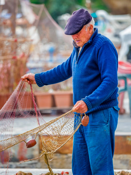 Procida Island in the Campania region of Italy on October 26, 2017: Elderly fisherman  mending traditional fishing nets by hand on Procida Island harbor