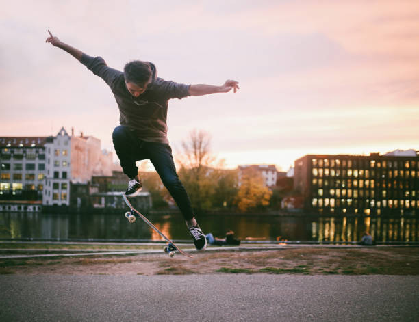 A happy teenage boy in casual clothes and with a skateboard in his hands is standing in a skateboard park and looking at the camera
