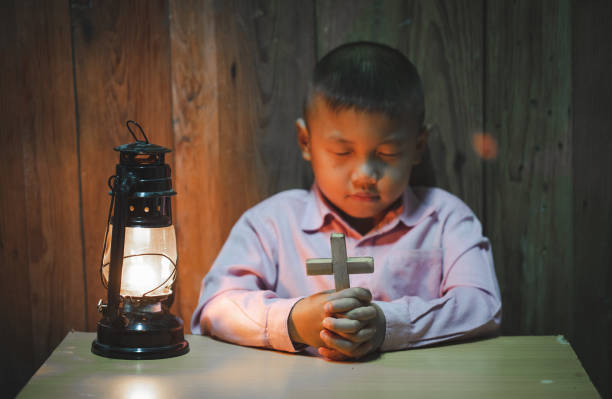 мальчик руки молятся со святым крестом в темноте и с лампой рядом, ребенок молится за бога религии. - praying human hand worshipper wood стоковые фото и изображения