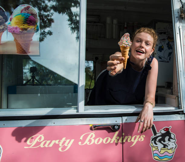 Smiling female ice cream vendor sells ice cream cone topped with multi color sprinkles Smiling young female ice cream vendor holds out an ice cream cone topped with multi color sprinkles. The pretty young woman leans out of a pink retro style ice cream van in Sydney, Australia. ice cream van stock pictures, royalty-free photos & images