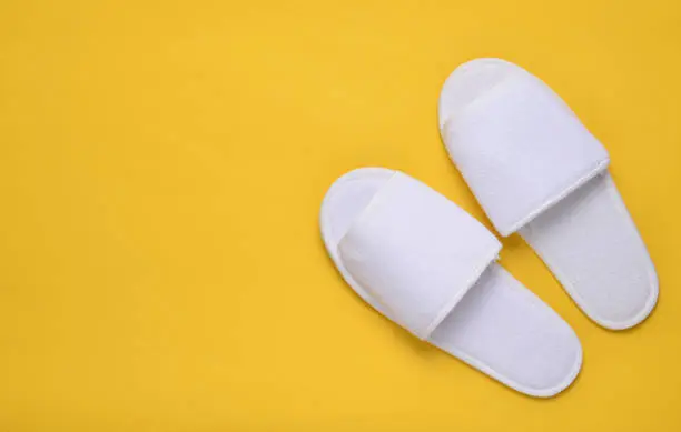 White hotel slippers on a yellow background, top view, minimalist trend