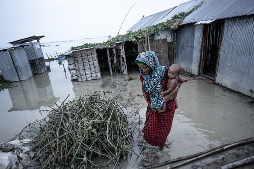 A woman is walking with her child amid a flooded land in Khaliajuri,Bangladesh; flood creates massive food crisis in these areas; milk becomes scarce and the children suffer from malnutrition.