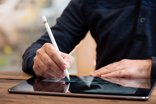 Close-up of a woman's hand writing or signing a document on a digital tablet with a stylus