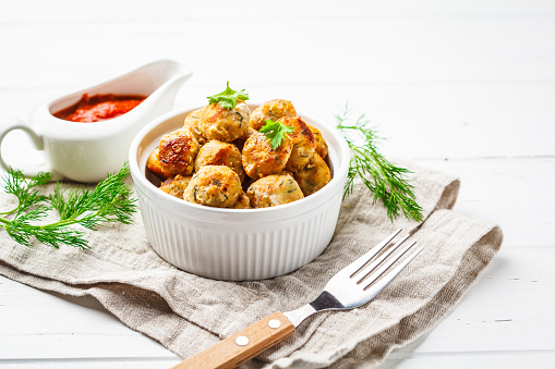 Healthy chicken meatballs with greens and tomato sauce on a white background.