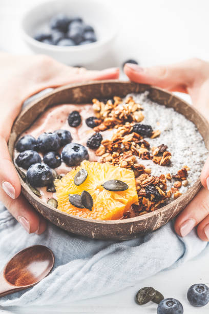 istock Breakfast smoothie bowl with chia pudding, berries and granola in a coconut shell on white wooden background. 1088884826