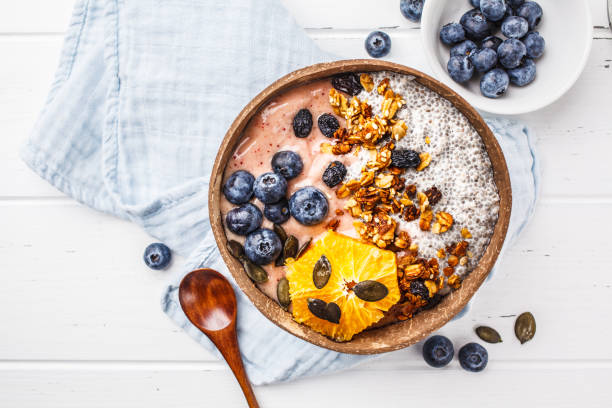 istock Breakfast smoothie bowl with chia pudding, berries and granola in a coconut shell on white wooden background. 1088884856