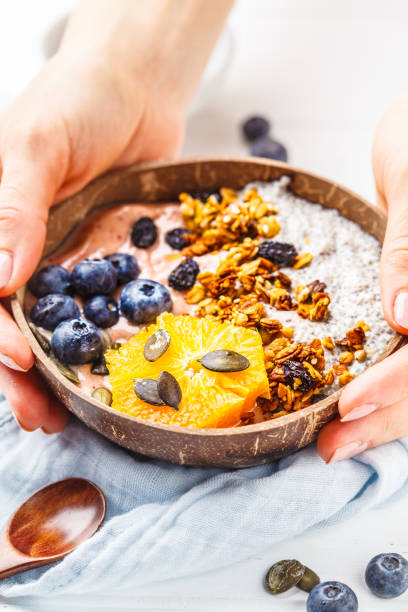istock Breakfast smoothie bowl with chia pudding, berries and granola in a coconut shell on white wooden background. 1088884880
