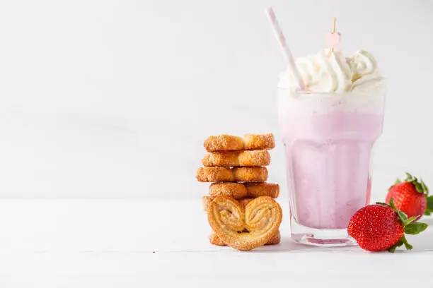 Strawberry milkshake with whipped cream and cookies Palmiers on a white background, copy space for text. Valentine's day concept.