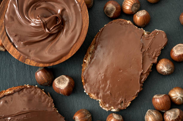 top view of hazelnut chocolate spread, sliced bread and hazelnuts on black stone background - chocolate spread imagens e fotografias de stock