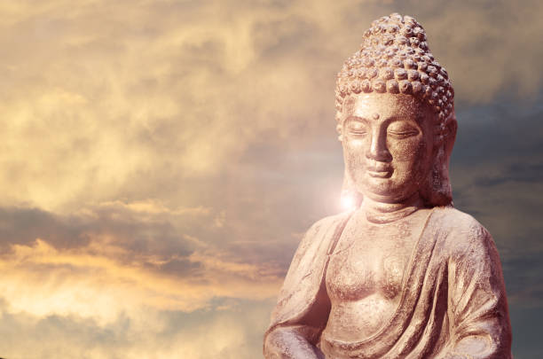 istock Buddha statue sitting in meditation pose against sunset sky with golden tones clouds. 1088903786