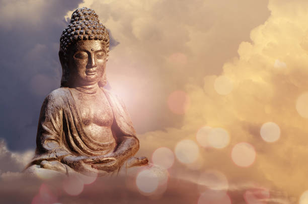 istock Buddha statue sitting in meditation pose against sunset sky with golden tones clouds. 1088903814