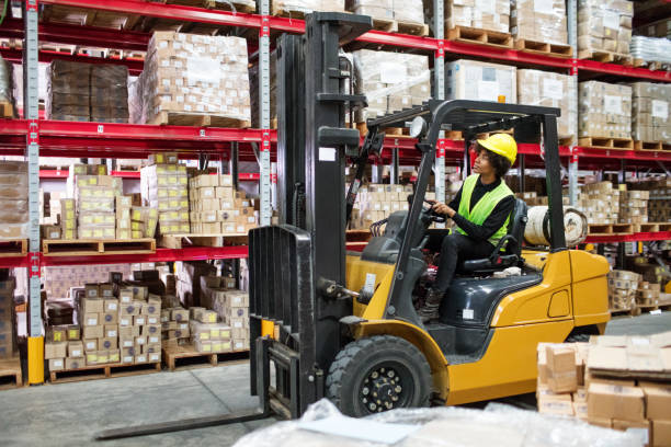 Woman driving forklift in warehouse Woman driving forklift carefully through aisle in warehouse. Female worker driving forklift in warehouse. forklift photos stock pictures, royalty-free photos & images