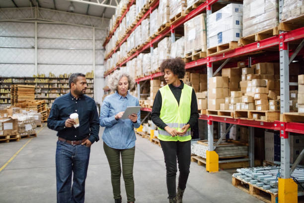 warehouse manager walking and talking with team Senior manager using digital tablet while walking in warehouse with supervisor and foreman. Manager walking and talking with workers in warehouse. hardware store photos stock pictures, royalty-free photos & images