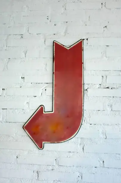 Photo of left arrow sign on white brick wall, block background with arrow sign