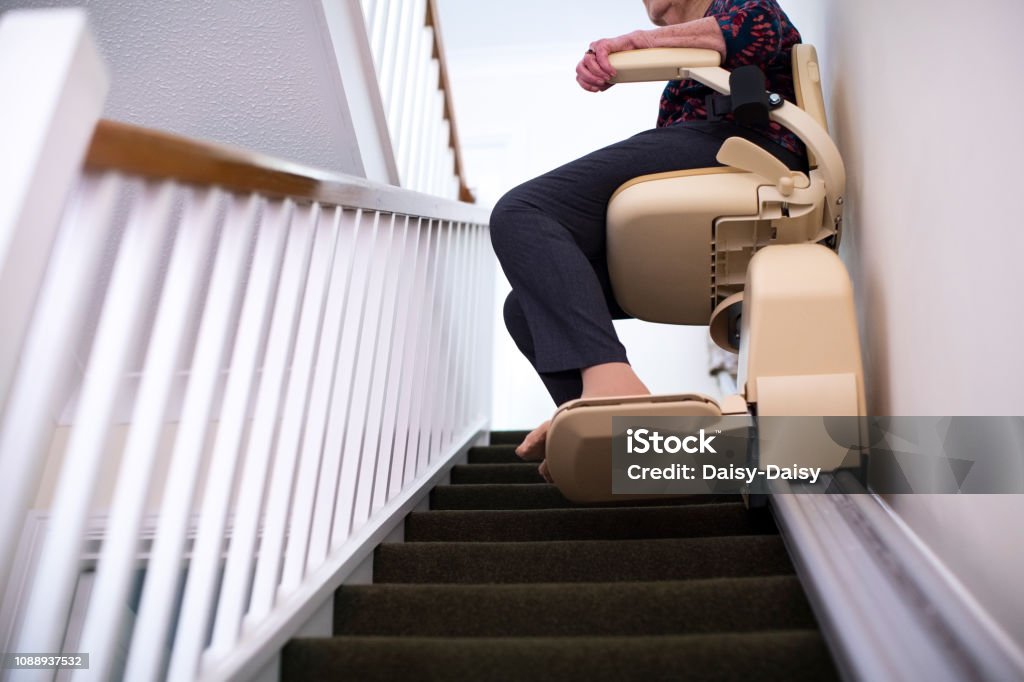 Detail Of Senior Woman Sitting On Stair Lift At Home To Help Mobility Stair Lift Stock Photo