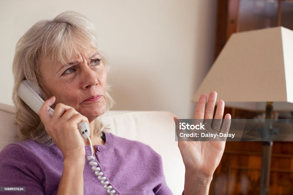 Mulher sênior recebendo telefonema indesejado em casa - Foto de stock de Telefone royalty-free