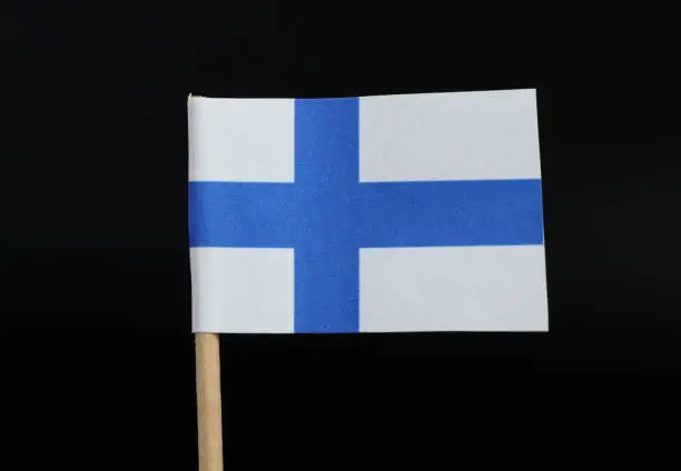 A official flag of Finland on toothpick on black background. Consists of Sea-blue Nordic cross on white field.