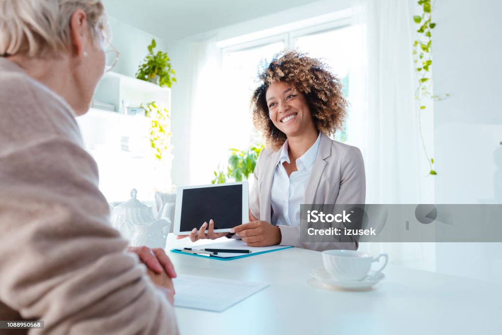 Female financial advisor talking with senior woman Cheerful female advisor talking with senior woman, holding digital tablet in hands. Diabetes Stock Photo