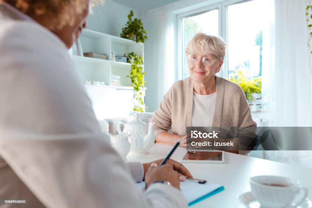 Senior woman talking with financial advisor Smiling senior woman talking with insurance advisor, sitting at the table in living room together. Nutritionist Stock Photo