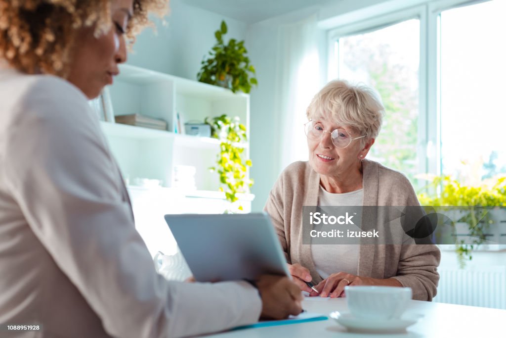 Senior woman talking with financial advisor Smiling senior woman talking with insurance advisor, sitting at the table in living room together. Diabetes Stock Photo