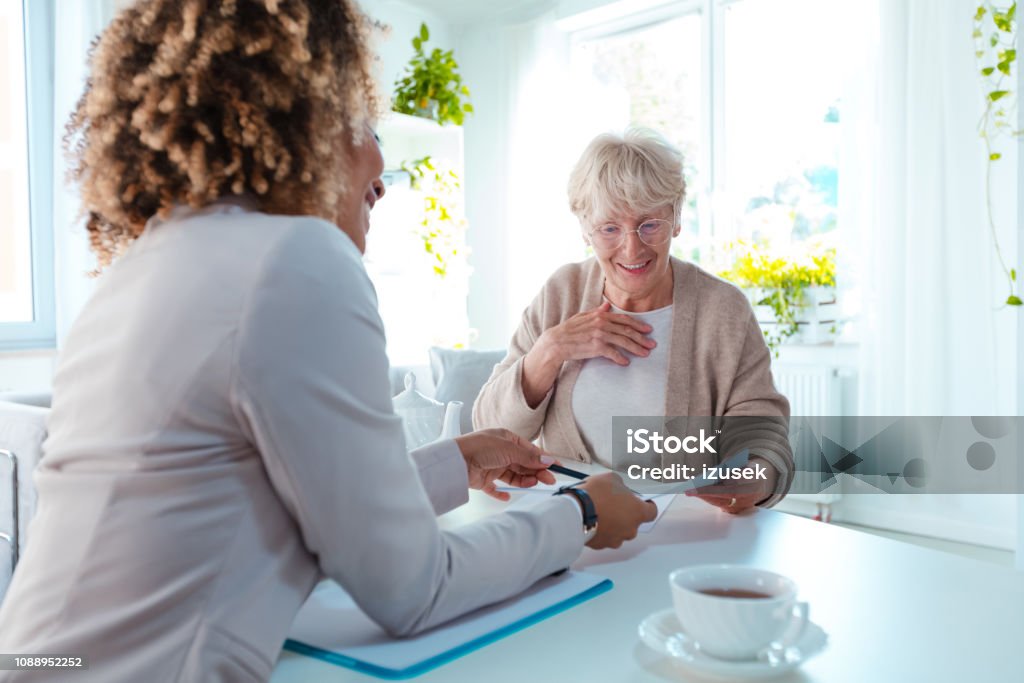 Senior woman talking with financial advisor Happy senior woman talking with insurance advisor, sitting at the table in living room together. Senior Adult Stock Photo