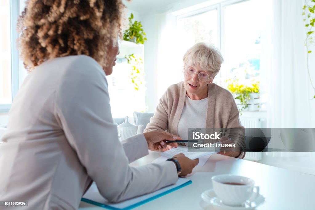 Senior woman talking with nutritionist Senior woman talking with dietician, consulting her diet plan, sitting at the table in living room together. Assistance Stock Photo