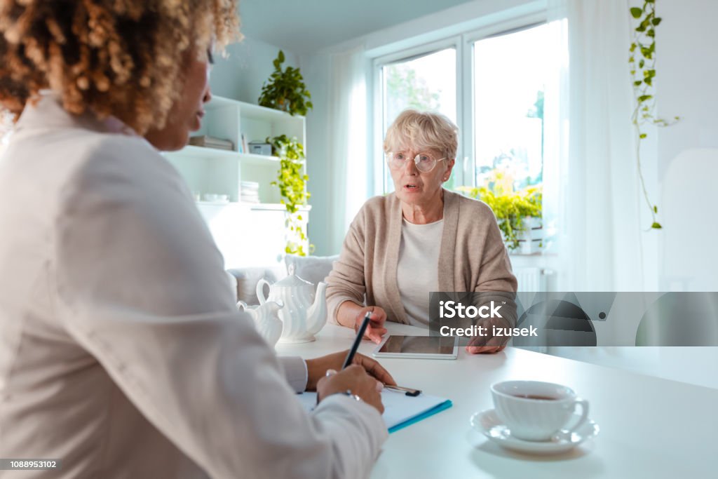 Worried senior woman talking with financial advisor Worried senior woman talking with insurance advisor, sitting at the table in living room together. A Helping Hand Stock Photo Worried senior woman talking with financial advisor Worried senior woman talking with insurance advisor, sitting at the table in living room together. A Helping Hand Stock Photo