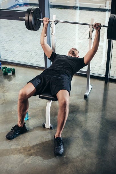 istock handsome sportsman lifting barbell with weights while lying on bench in gym 1088957892