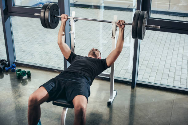 istock handsome sportive man lifting barbell with weights while lying on bench in gym 1088957912