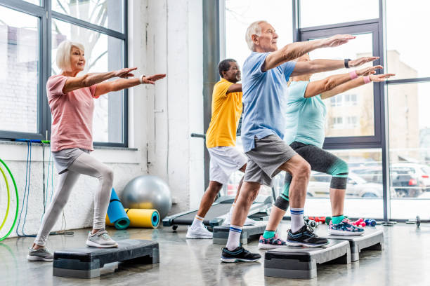 atletas seniors sincrónicos de ejercicio sobre plataformas de paso en el gimnasio - aerobics fotografías e imágenes de stock
