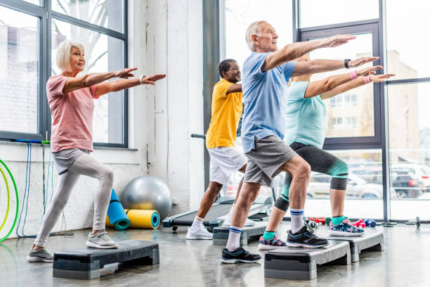 senior athletes synchronous exercising on step platforms at gym - aerobics imagens e fotografias de stock