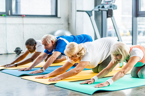 cheerful senior athletes synchronous exercising on fitness mats at gym