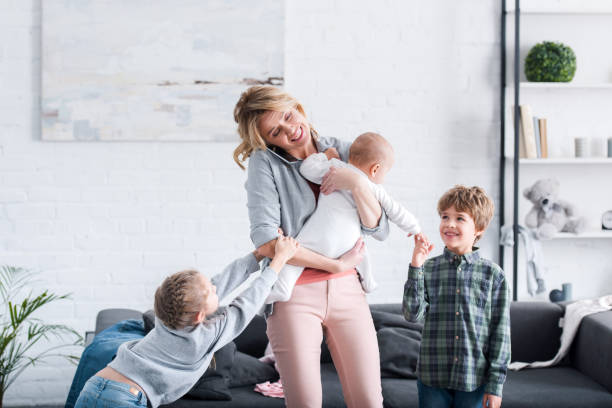 istock exhausted mother talking by smartphone and holding infant child while naughty siblings playing in room 1088961212