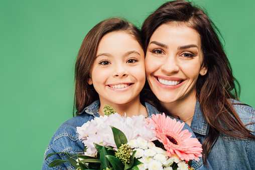 portrait of happy mother and daughter with flowers isolated on green