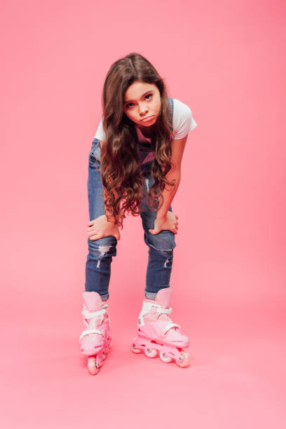istock upset child in overalls and rollerblades pouting lips and looking at camera on pink background 1088963920