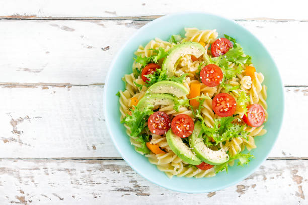 Pasta salad with avocado, fresh tomato, pepper and lettuce, top view