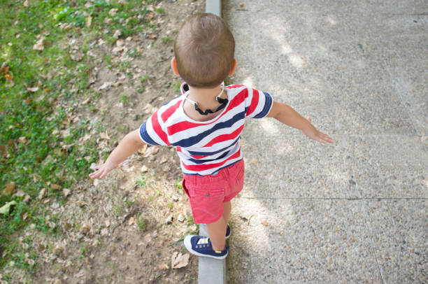 Toddler boy performing as tightrope walker on garden curb. Training balance for kids concept