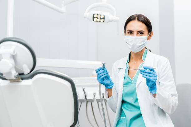 female dentist in white coat and mask holding dental instruments stock photo