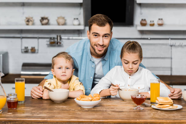 istock smiling father looking at camera and embracing siblings eating porridge at table 1088971238