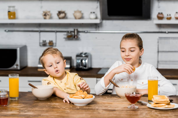 istock cute siblings sitting at table and holding cookies 1088971248