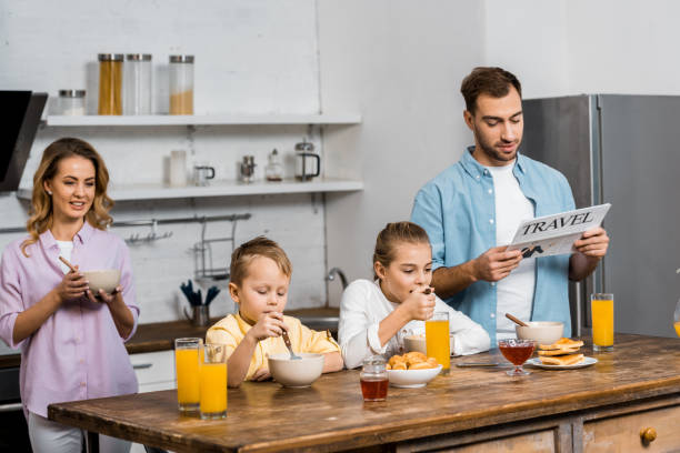 息子と娘の父の読んでいる間オートミールを食べて旅行の台所新聞 - newspaper reading mother women ストックフォトと画像