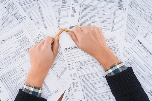 cropped view of stressed man breaking pencil with tax forms on background