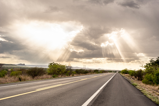 Road crossing at sertao (caatinga biome) covered by clouds into light beams, near Arcoverde city, Pernambuco state. BR 232 national highway. Brazilian transportation infrastructure
