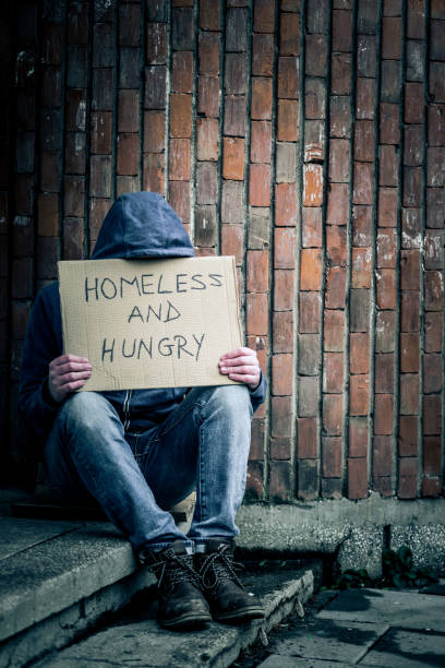 istock Young Homeless Depressed Man Sitting Outdoors holding Cardboard Sign 1088995708
