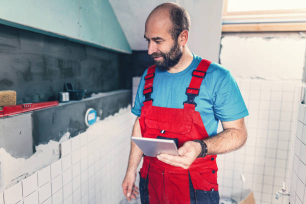 Qualified tiler browsing on his tablet while installing tiles in the bathroom Tile professional working in the bathroom and reviewing the project on his tablet qualified report stock pictures, royalty-free photos & images