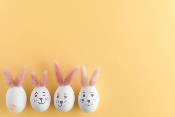 istock Top view of Easter eggs making with pink bunny ears in different patterns. Pastel yellow background. Copy space. 1089006564
