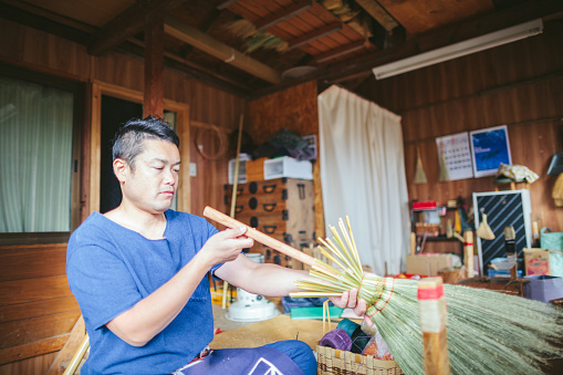 An Asian man is making brooms in his working place.