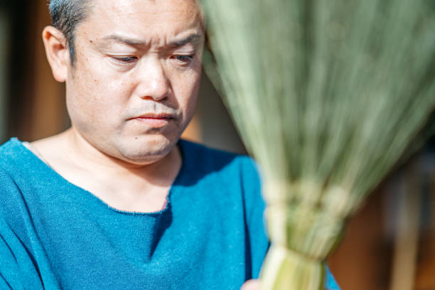An Asian man is making brooms in his working place.