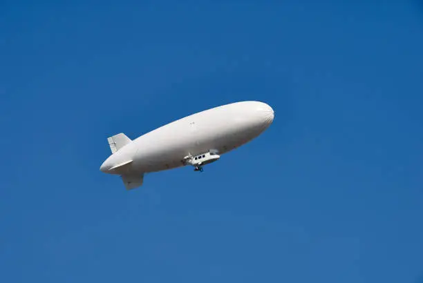 Photo of Large white dirigible airship against a clear blue sky. Plenty of room for text.