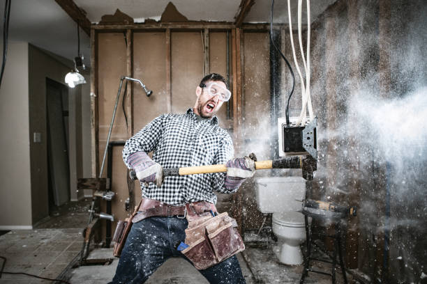 Contractor Man Doing Home Improvement and Demolition A man attempts to work on renovating his home, with funny and disastrous results.  He swings a sledgehammer, taking out part of a wall. demolished stock pictures, royalty-free photos & images
